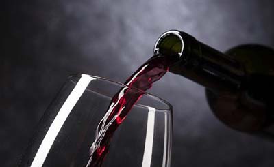Aus einer grünen Weinflasche wird Rotwein in ein durchsichtiges Weinglas geschüttet.