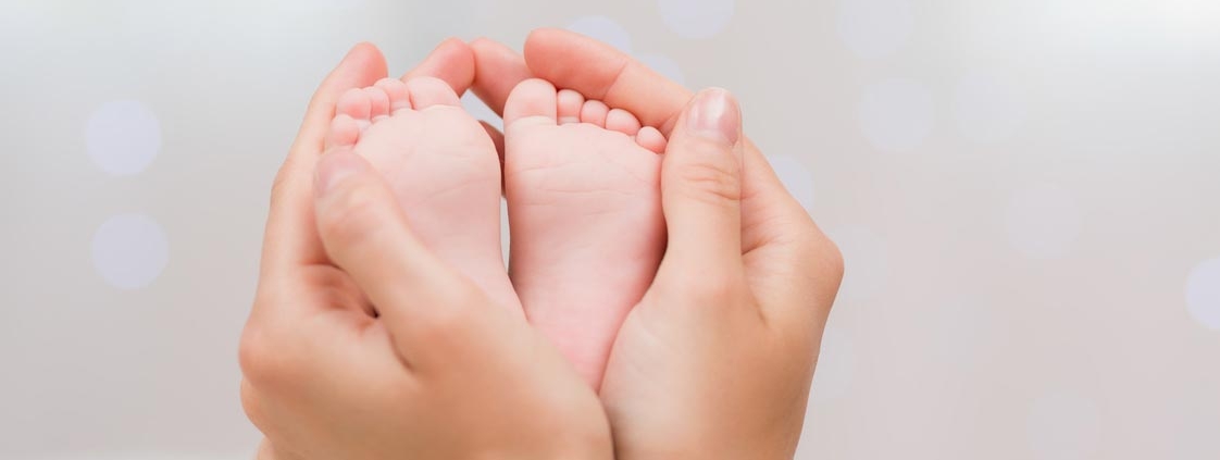 Zarte Mutterhände umfassen die Füße eines Babys. Die Fußsohlen sind zu sehen, außen die Hände.